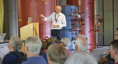 Mann hält Präsentation vor Menschen mit Energiespeichern im Hintergrund
