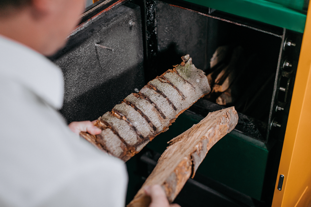 Person am Einheizen mit Stückholz vor Holzheizung